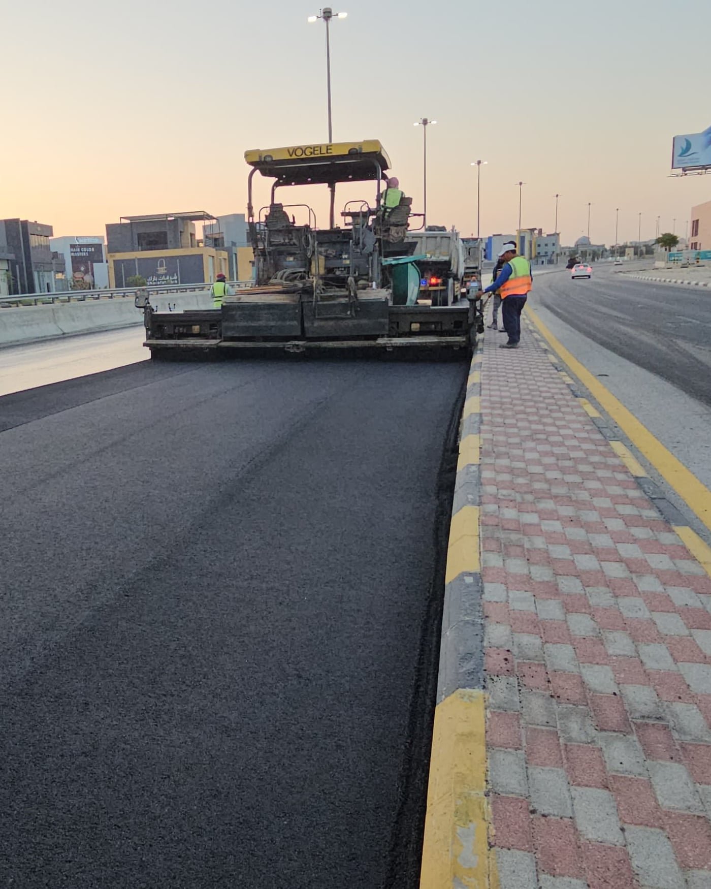 Asphalt paver and crew at work at golden hour